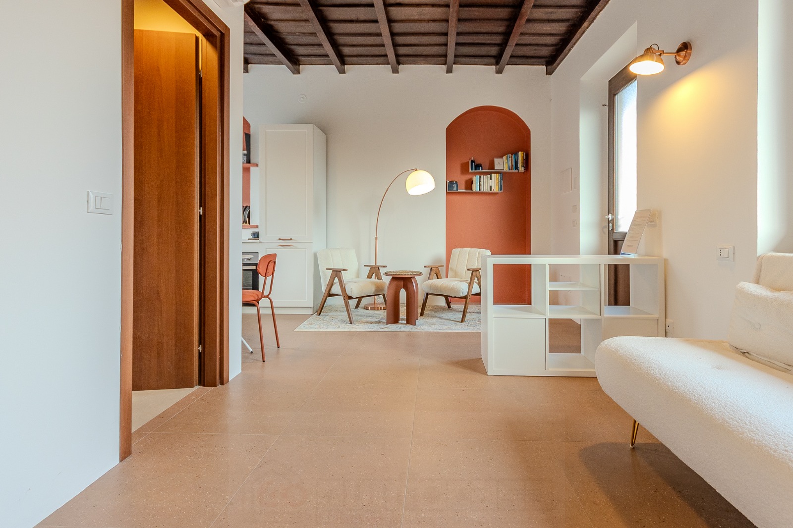 Soggiorno con nicchia ad arco color terracotta, libreria, due poltroncine in bouclé chiaro e lampada ad arco — Il Cortile della Birona, Monza