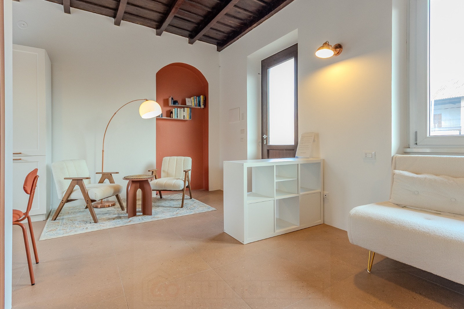 Soggiorno del Cortile della Birona con soffitto a travi a vista, nicchia ad arco in terracotta e arredi in bouclé