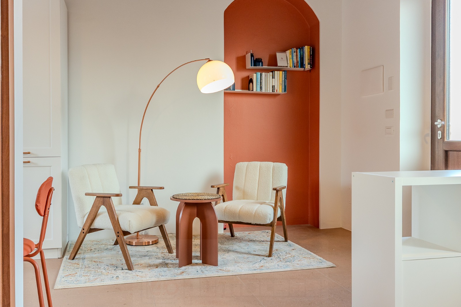 Angolo lettura con due poltroncine in bouclé chiaro e lampada ad arco davanti alla nicchia in terracotta con libreria