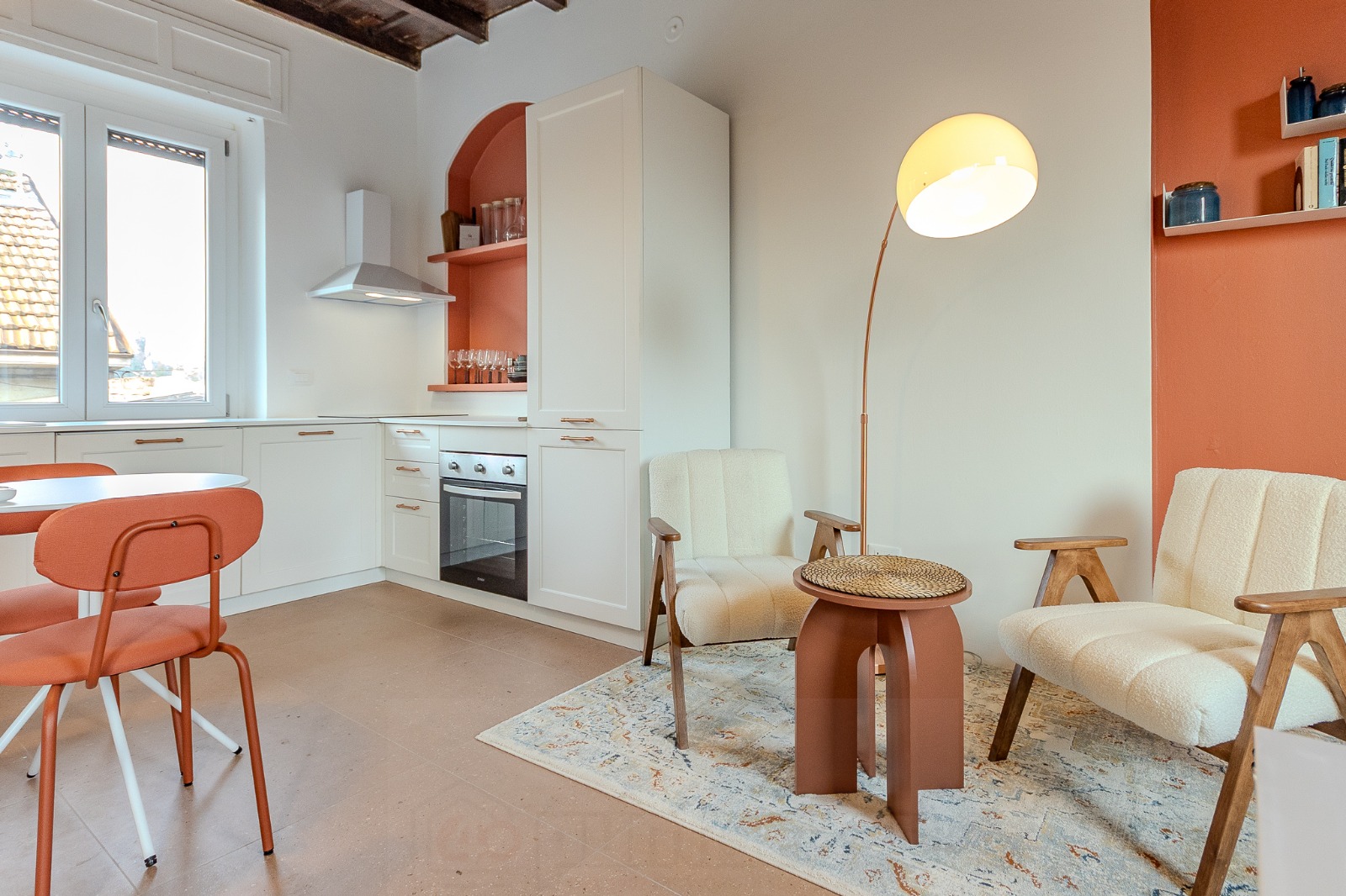 Vista d'insieme del soggiorno del Cortile della Birona con zona pranzo, sedie terracotta e cucina bianca