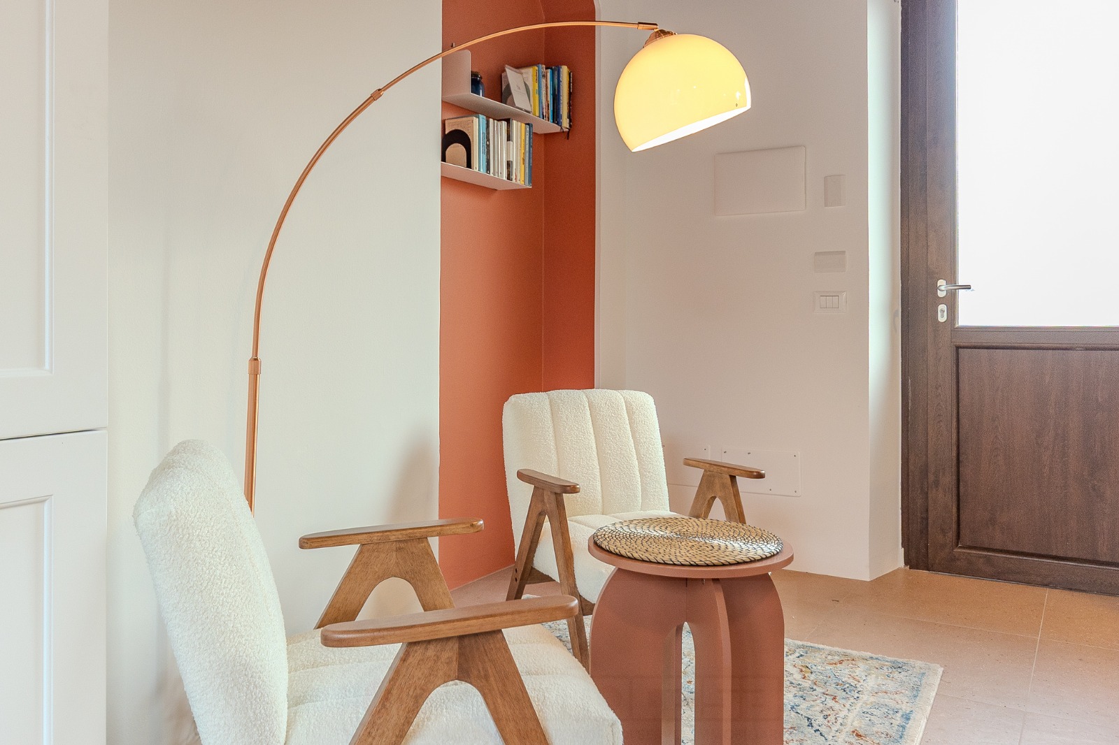 Dettaglio del soggiorno con poltroncine in bouclé, lampada ad arco in rame e nicchia in terracotta